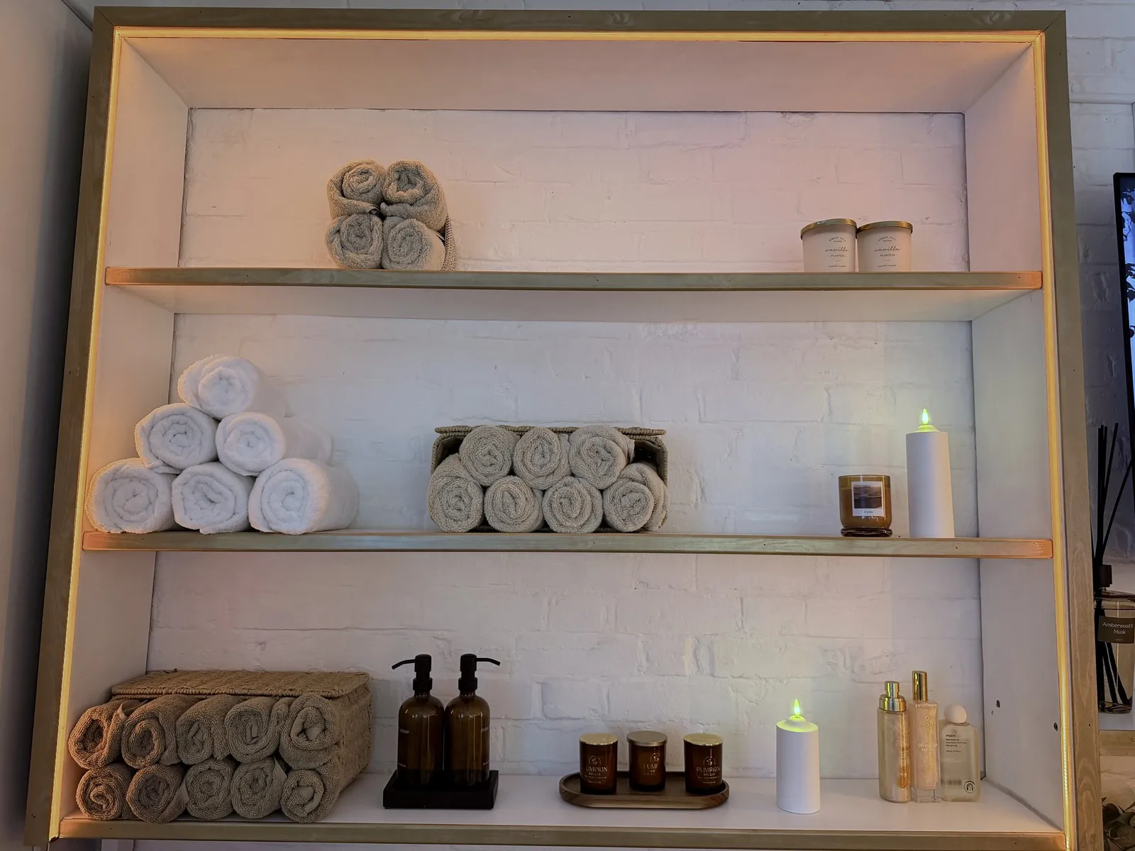 Gold-trimmed studio shelves arranged with rolled towels, candles and skincare