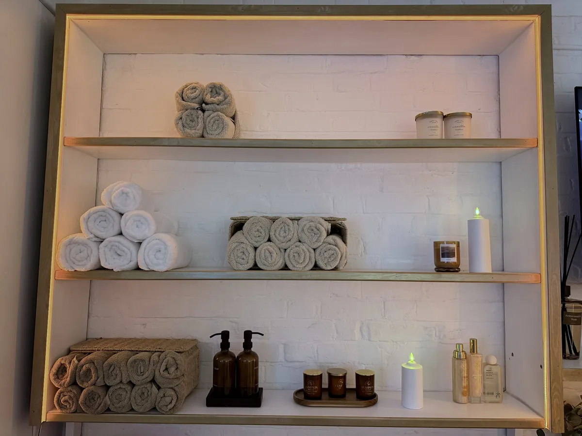 Gold-trimmed shelves with rolled towels, candles and skincare in the finished Vora Wellness studio