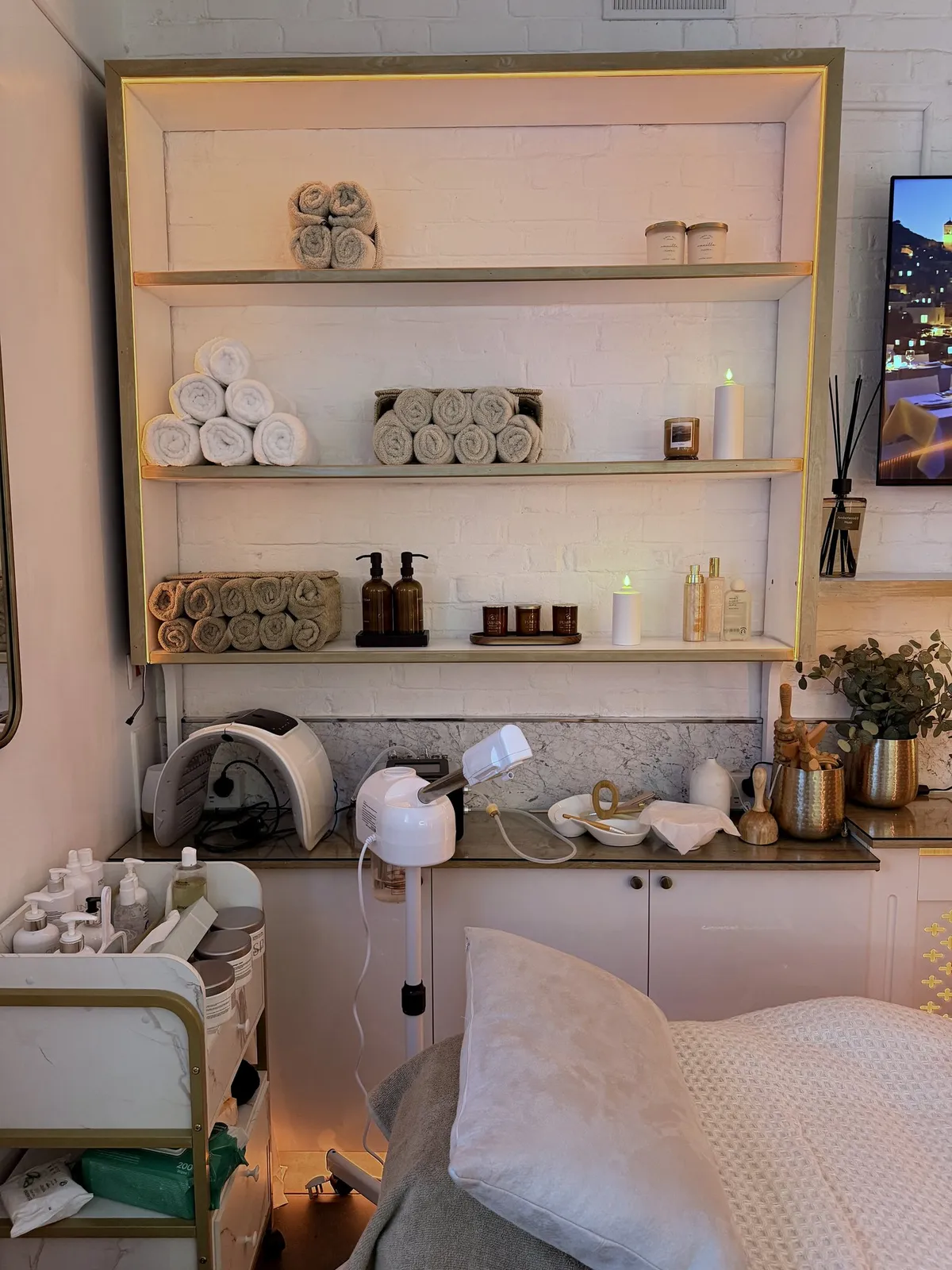 The treatment room at Vora Wellness, with its linen-covered bed and gold-trimmed shelving